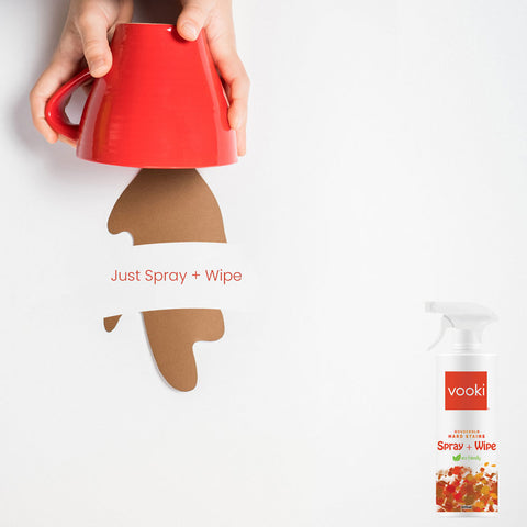 A hand holding a red cup with a brown coffee stain marks, by displaying vooki hardstain spray+wipe bottle